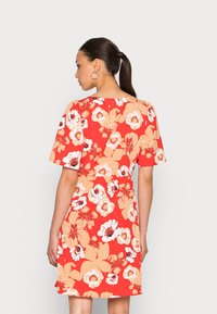 Vestido floral vermelho com um design de mangas curtas. Apresenta grandes flores brancas e bege sobre um fundo vibrante, feito de um tecido suave.