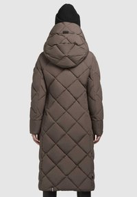 Lang, brun dunfrakke med et diamantquiltet mønster og en stor hætte. Stoffet ser glat ud og har sidelommer. Accepteret med en sort strikhat.