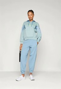 Svetlo modra majica s kapuco in ribastim robom, v kombinaciji z ujemajočimi se trenirkami, ki imata oboje mehak teksturo in športne oblikovalske elemente.