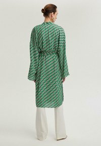 Roheline mustriga kimono-stiilis rüü, millel on pikad varrukad ja mis on vööga seotud, esitleb geomeetrilist mustrit. Kantakse koorevärvi pükste peal.