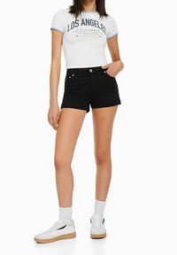 Shorts en denim noir avec ourlets retroussés, associés à un crop top blanc avec des accents bleus et des baskets noires avec une semelle en gomme.