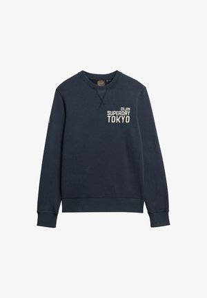 Navyblauwe crewneck sweatshirt met een gestructureerde afwerking. Voorzien van een geborduurd "Tokyo" logo en accent op de mouw. Ribbelboord aan de hals en manchetten.