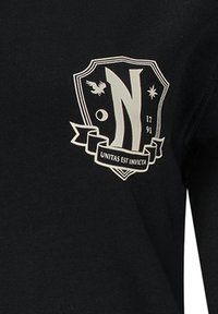 Czarna koszulka z długim rękawem z białym logo w kształcie tarczy, zawierającym stylizowane "N", orła, gwiazdę, piłkę nożną oraz wstęgę z napisem.