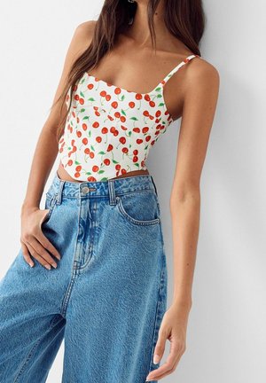 Biały krótki top w czerwony wzór z wiśniami, na cienkich ramiączkach, zestawiony z jasnoniebieskimi, szerokimi dżinsami o wysokim stanie i wyraźnej fakturze.
