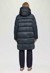 Zwarte pufferjas met capuchon, met een gewatteerd ontwerp, midden-dij lengte en geribde manchetten. Gepaard met donkere denim broek en sneakers.