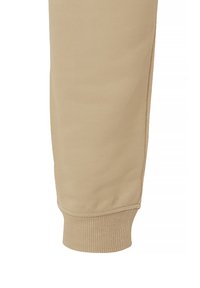 Beige Baumwoll-Jogginghose mit einem gerippten Bund, glatter Textur und taillierter Form. Naht an der inneren Oberschenkelseite sichtbar.