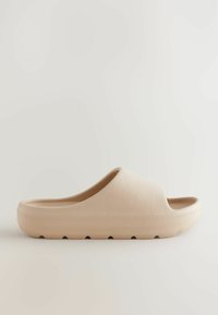 Sandale beige à enfiler avec une surface texturée et un design arrondi. Semelle légèrement surélevée avec de petites indentations pour une meilleure adhérence.