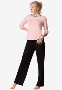 Różowa bluzka z rękawami 3/4 i czarnym wykończeniem, w połączeniu z czarnymi spodniami o szerokich nogawkach. Oba elementy charakteryzują się gładką, miękką fakturą materiału.