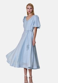 Robe midi bleu clair en tissu respirant, dotée de manches bouffantes, d'un col en V, d'une taille nouée, et d'accents floraux sur le côté.