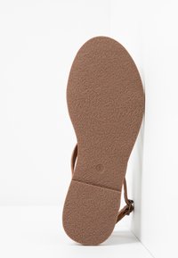 Semelle en caoutchouc marron avec surface texturée et design plat. Détail minimaliste de bride visible au talon, sans accents ou caractéristiques supplémentaires.