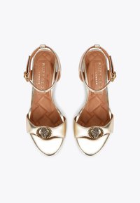 Złote metaliczne sandały na obcasie z szerokim paskiem, zapięciem na kostkę oraz ozdobnym zapięciem, z teksturowaną wkładką i pikowanym wzorem.