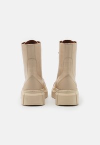Bottes courtes en cuir beige avec une semelle épaisse, présentant une texture lisse, des détails cousus et un design minimaliste.