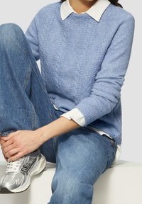 Maglione a maglia blu chiaro con un motivo a diamante testurizzato, indossato sopra una camicia bianca con colletto. Abbinato a jeans e scarpe sportive argento.