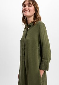 Langärmliges, olivgrünes Hemdkleid aus leichtem, strukturiertem Stoff. Verfügt über einen Knopfkragen und seitliche Taschen für Funktionalität.