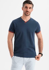 Námořnická v-neck tričko s červenými akcenty na límci a rukávech. Vyrobené z měkké tkaniny, s krátkými rukávy a přiléhavým designem.