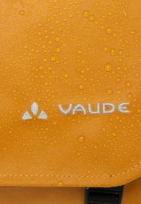 Tessuto arancione resistente all'acqua con gocce d'acqua, caratterizzato dal logo bianco "Vaude" e da un emblema geometrico. Texture liscia con bordo cucito.