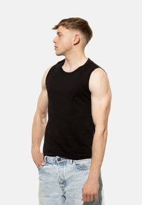 Top senza maniche nero in cotone, con scollo rotondo e vestibilità aderente, abbinato a jeans in denim blu chiaro.
