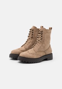 Botas de tobillo de ante marrón con cordones en la parte delantera, detalles de brogue, punta redonda y una gruesa suela de goma negra. Incluyen tiradores para facilitar su puesta.