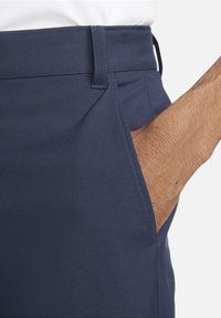 Navy blue trousers with a smooth texture, featuring a front pocket detail and a slim fit design. Stitched waistband with belt loops visible.