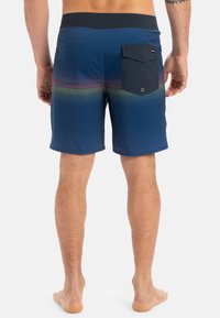 Shorts de bain navy avec un motif rayé horizontal en dégradés, taille élastique, et une poche arrière avec un rabat et une fermeture à bouton.