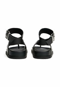 Sandali neri con suola piatta, presentano ampie cinghie incrociate e chiusura con fibbia. Materiale sintetico liscio con design open heel.