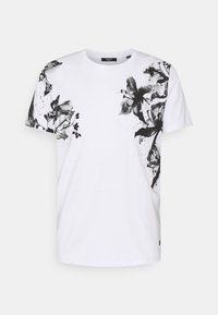 T-shirt de algodão branco com um design de impressão floral preta no lado esquerdo, com mangas curtas e decote redondo.
