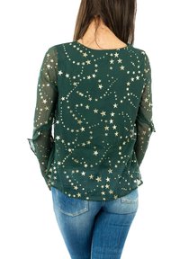 Grön genomskinlig blus med guldstjärnmönster, lång ärm och en lätt volangkjol, kombinerad med blå denimjeans.