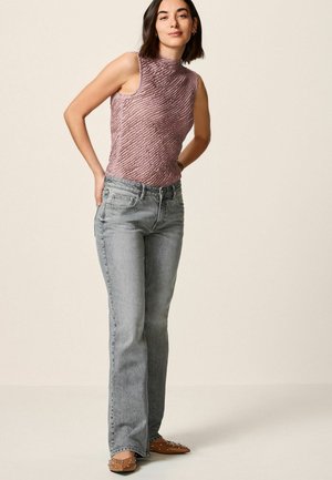 Hellrosa, strukturierte, ärmellose Bluse mit hohem Kragen, kombiniert mit hellgrauen, ausgestellten Jeans und beigen Mules mit Nieten. Neutraler Hintergrund.