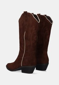 Botas de cowboy de ante marrón con parte superior con ondas, costuras decorativas y un tacón bajo. Cuentan con un zipper lateral y una textura suave.