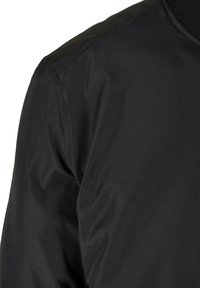 Chaqueta bomber negra hecha de tela suave y ligera. Presenta un cuello de canalé y costuras visibles a lo largo del hombro.