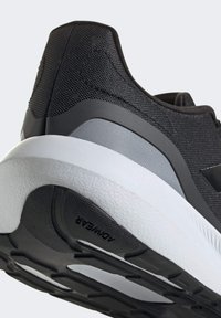 Zapatilla deportiva negra con parte superior de malla texturizada, entresuela gris y suela exterior de goma duradera con un diseño apilado y una banda de rodadura con patrón.