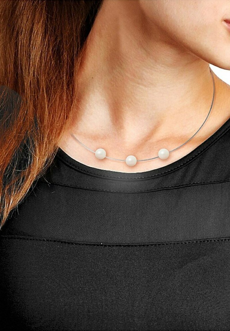 Collier en fil d'argent avec trois perles rondes blanches, positionnées uniformément le long de la longueur, reposant sur un haut noir. Design simple et minimaliste.