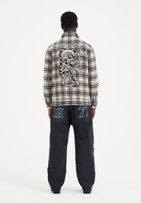 Black and white plaid jacket with a large embroidered dragon on the back, paired with dark denim pants featuring white numerical accents.