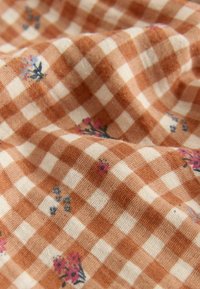 Tela a cuadros marrón y crema con patrones florales en tonos rosa y azul, que presenta una superficie suave y texturizada.