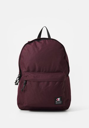Bordeauxfarbener Rucksack mit einem Reißverschluss-Hauptfach, Fronttasche, verstärktem Griff und einem schwarzen Logo-Aufnäher an der Unterseite. Strukturierter Stoff.
