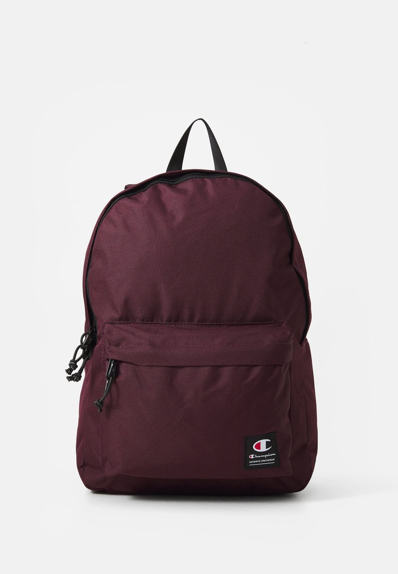 Mochila burdeos con un compartimento principal con cremallera, bolsillo frontal, asa reforzada y un parche de logotipo negro en la base. Tejido texturizado.