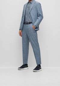 Abito a quadri azzurri con pantaloni abbinati, camicia blu navy, cintura nera e sneakers scure con dettagli verdi. Tessuto liscio, vestibilità su misura.