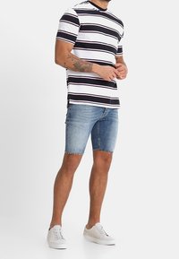 Camiseta de manga corta con rayas en blanco y negro con detalles en rosa, combinada con pantalones cortos de mezclilla azul claro y zapatillas blancas.