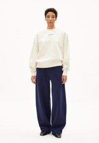 Witte sweatshirt met een ronde hals en verlaagde schouders, gecombineerd met marineblauwe wijde broekspijpen. Zwarte schoenen met studaccenten.