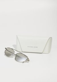 Occhiali da sole Michael Kors con lenti specchiate argento, montatura metallica e punte delle orecchie trasparenti. Include un astuccio bianco testurizzato con logo.