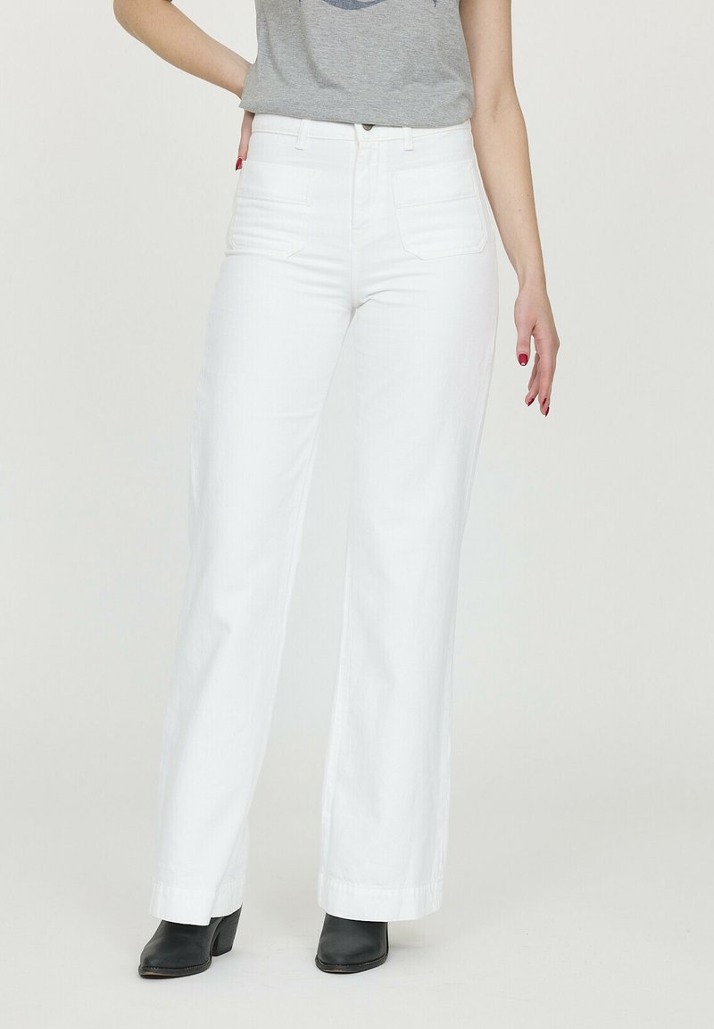 Jean large blanc à taille haute, en denim. Présente des poches avant et un ourlet soigné. Associé à un t-shirt graphique gris et des bottes noires.