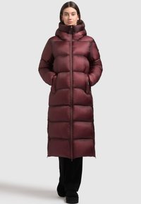 Dolga puffer jakna v temno burgundski barvi z visokim ovratnikom, horizontalnim quiltanjem in zadrgo spredaj. Ima stranske žepe in gladko, sijočo teksturo.