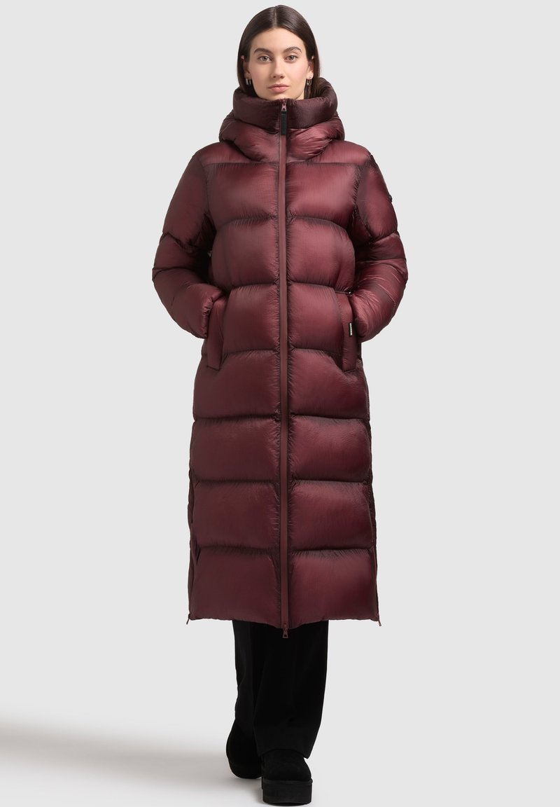 Dolga puffer jakna v temno burgundski barvi z visokim ovratnikom, horizontalnim quiltanjem in zadrgo spredaj. Ima stranske žepe in gladko, sijočo teksturo.