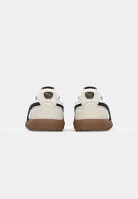 Hvide og sorte sneakers med en suede hælpanel, gummigummisål og PUMA-logo bagpå. Teksturerede overflader og kontrasterende farver er fremhævet.