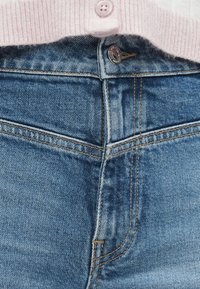 Ανοιχτό μπλε τζιν παντελόνι με χρυσές ραφές, διαθέτει κλείσιμο με κουμπί μπροστά και τσέπη στη δεξιά πλευρά. Απαλή υφή.