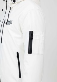 Giacca bianca con cappuccio, caratterizzata da zip e dettagli neri. Include una tasca a toppa sul braccio e un logo del marchio sul petto.