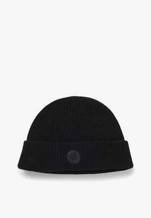 Bonnet en tricot noir avec une texture côtelée, comportant un patch logo noir rond à l'avant. Ajustement classique et snug.