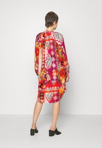 Värikäs mekko, jossa on kukkakuvio pinkki- ja punasävyissä, pitkät hihat ja rento leikkaus. Teksturoitu kangas ja polvenpituinen leikkaus.