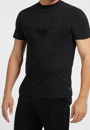 T-shirt noir en coton avec un logo triangulaire en relief sur la poitrine. Encolure ronde et manches courtes. Coupe ajustée, sans motifs apparents.