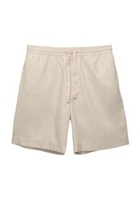 Shorts en coton beige avec une taille élastique, un cordon de serrage et des poches latérales. Présentent un design simple et une coupe décontractée. Texture unie.